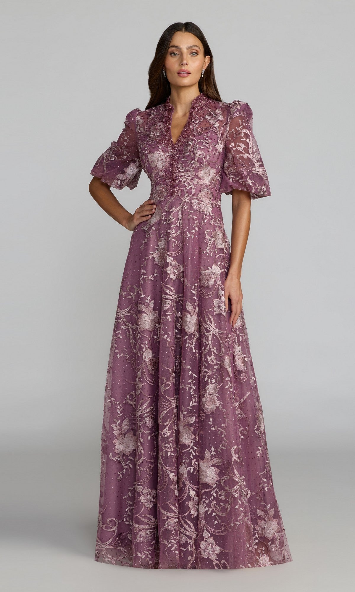 A woman wears the Mac Duggal 20452 Short Sleeve Beaded Formal Gown, featuring shimmering embellishments, as she stands against a plain light background.